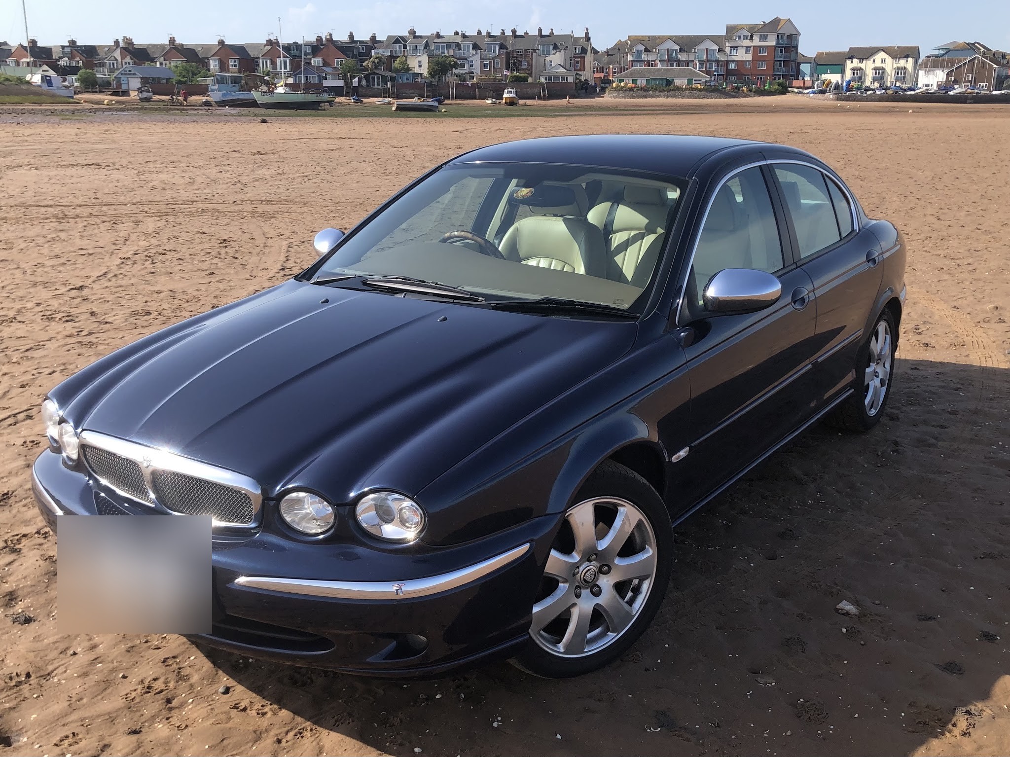 A customer's dark blue Jaguar X-Type parked on a beach