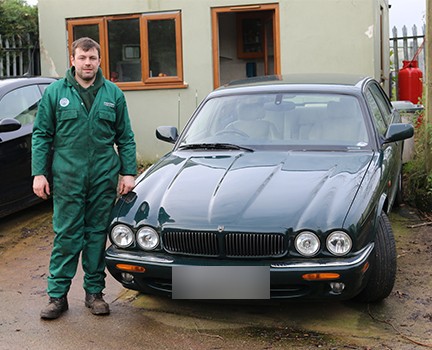 Liam Poll in LP Autotech overalls beside a green Jaguar XJ8 outside the workshop