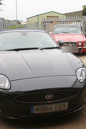 A black Jaguar XK with a red Jaguar XJ-S behind it in the yard