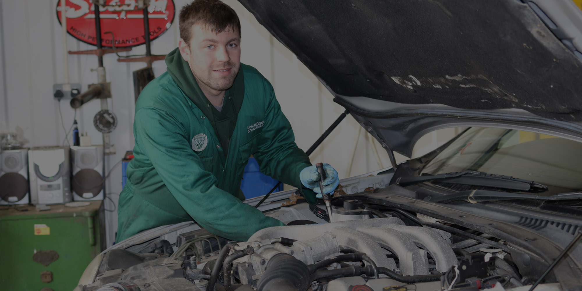 Liam Poll leaning into a Jaguar engine bay in the workshop
